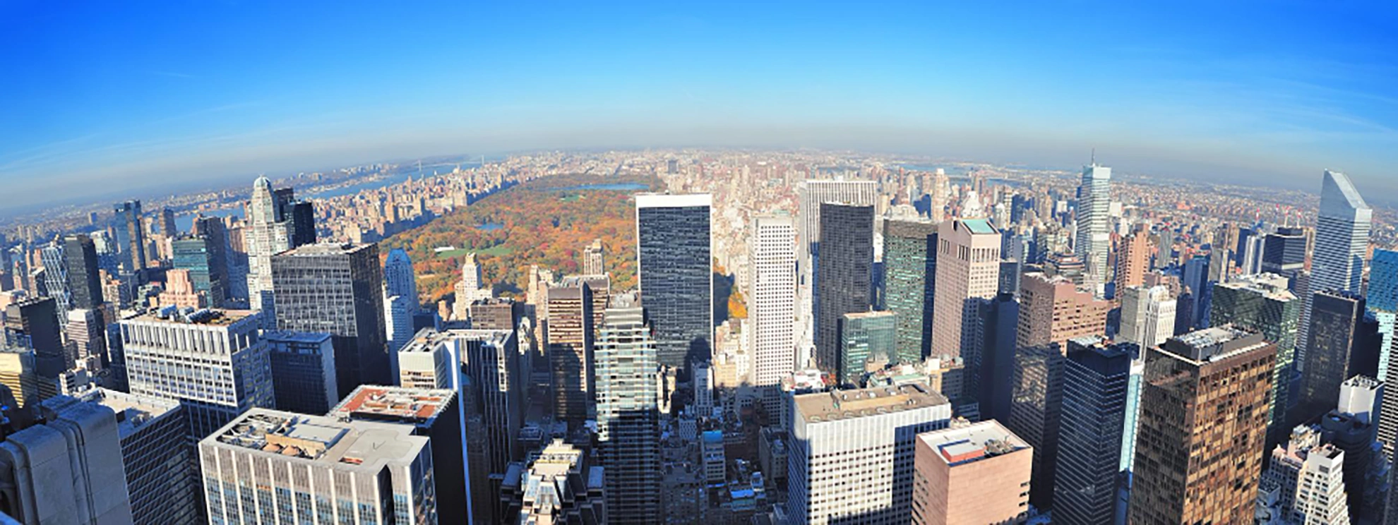 Aerial view of a city skyline with tall skyscrapers and a large park in the background under a clear blue sky