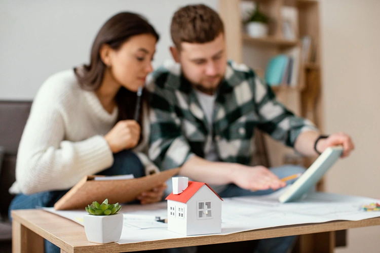 A couple reviewing documents together at a table with a small model house in the foreground
