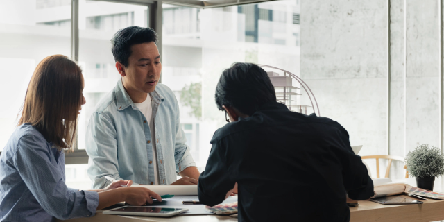 三个人聚在桌旁摊开纸张和书写工具进行讨论