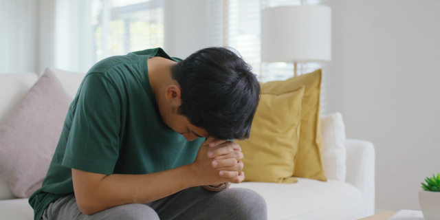 年轻男子坐在沙发上抱拳烦恼