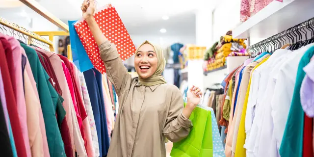 Wanita tersenyum sambil memegang beg membeli-belah melambangkan gaya hidup moden dan tahap literasi kewangan rakyat Malaysia yang mempengaruhi corak perbelanjaan.