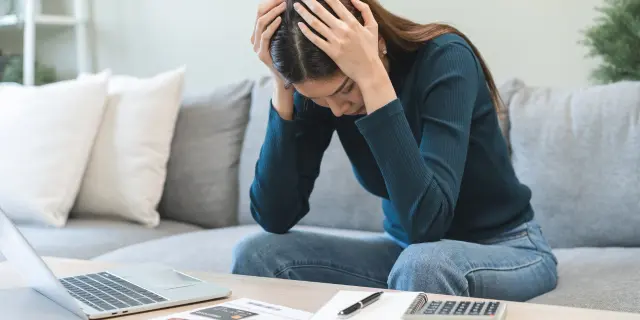 Wanita kelihatan tertekan di hadapan komputer riba dan bil kewangan, melambangkan tekanan kewangan rakyat Malaysia akibat beban hutang dan aliran tunai tidak stabil.